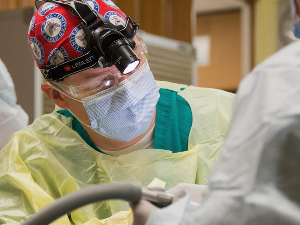 Surgeon wearing surgical cap and mask performing procedure.
