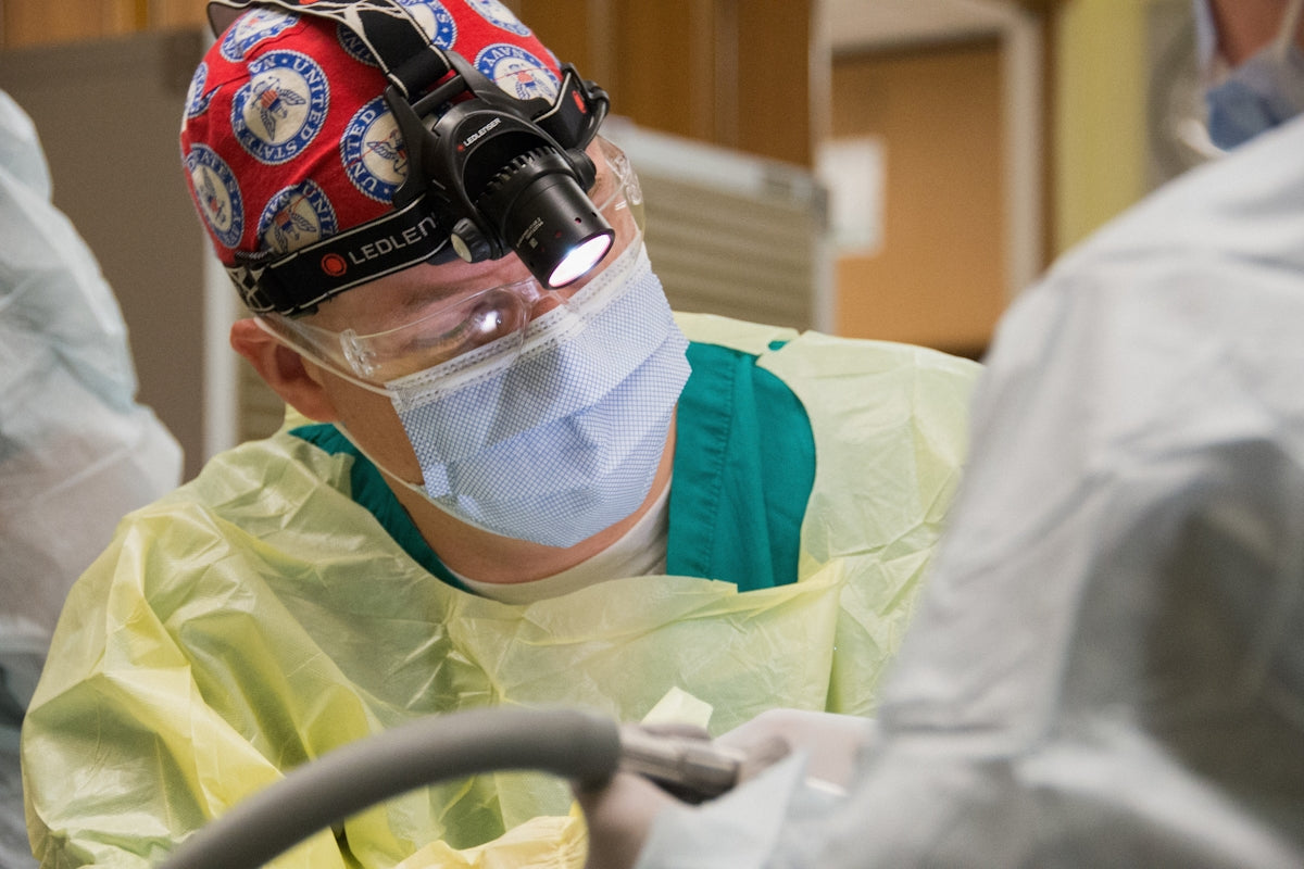 Surgeon wearing surgical cap and mask performing procedure.